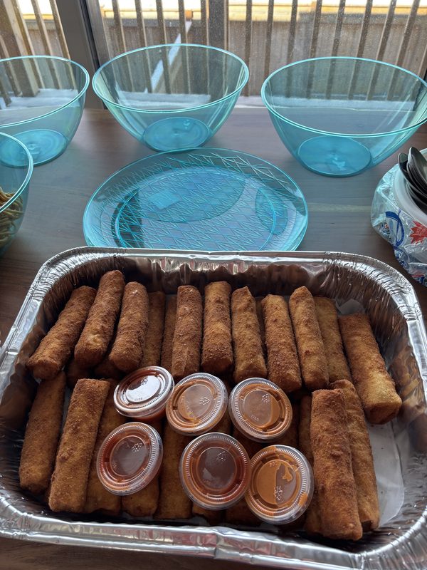 A tray of golden butter chicken rolls with cups of dipping sauce