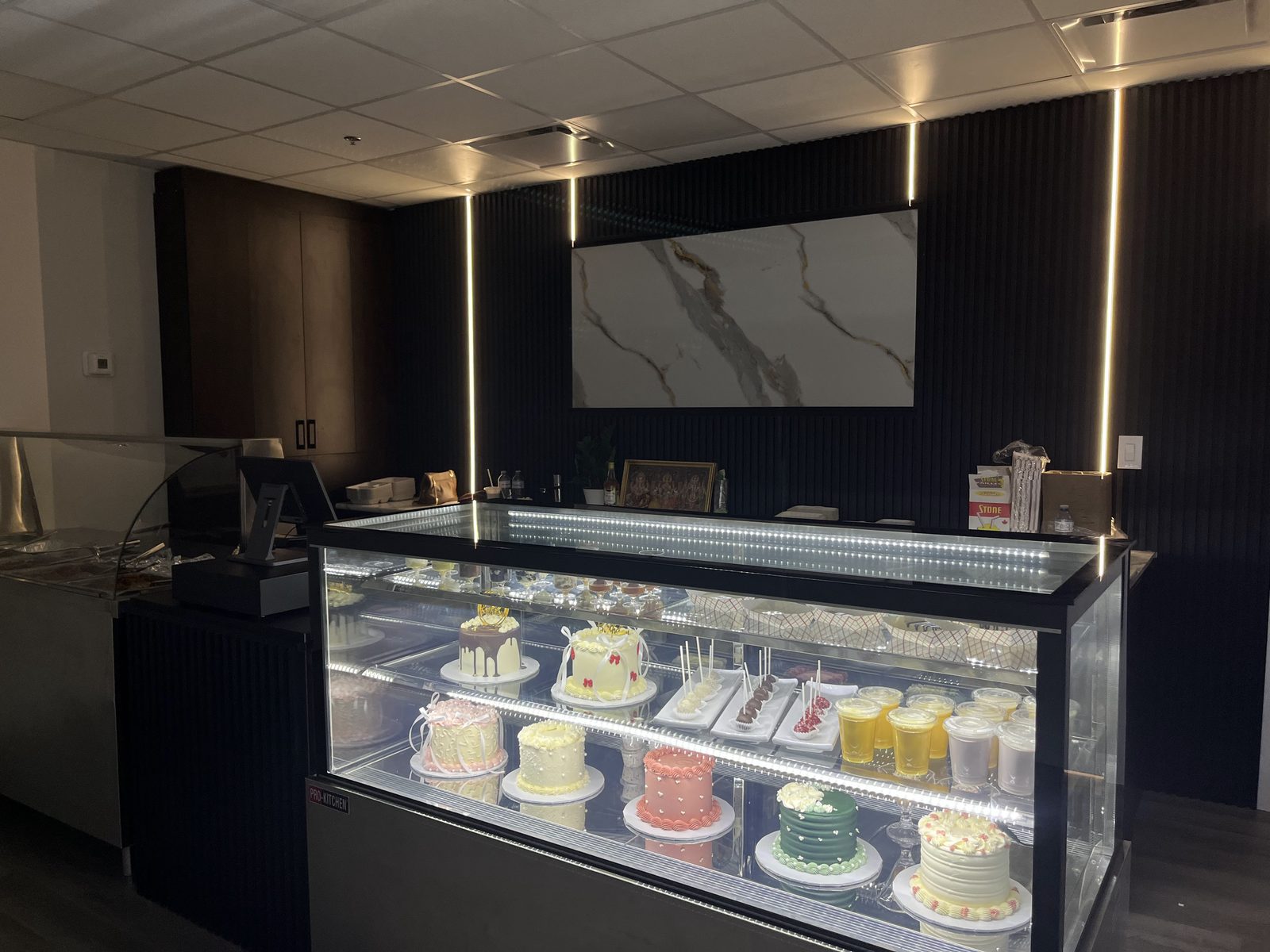 The cake case at Nisha's Culinary: rosette cakes, cake pops and dessert cups on lit glass shelves