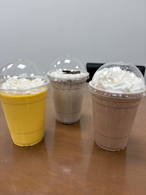 Three shakes with whipped cream in domed cups, the mango shake in front