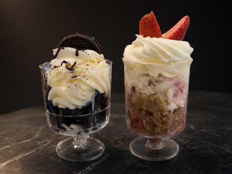 Two dessert cups: cookies and cream with a chocolate cookie on top, and strawberry with cream and strawberry halves