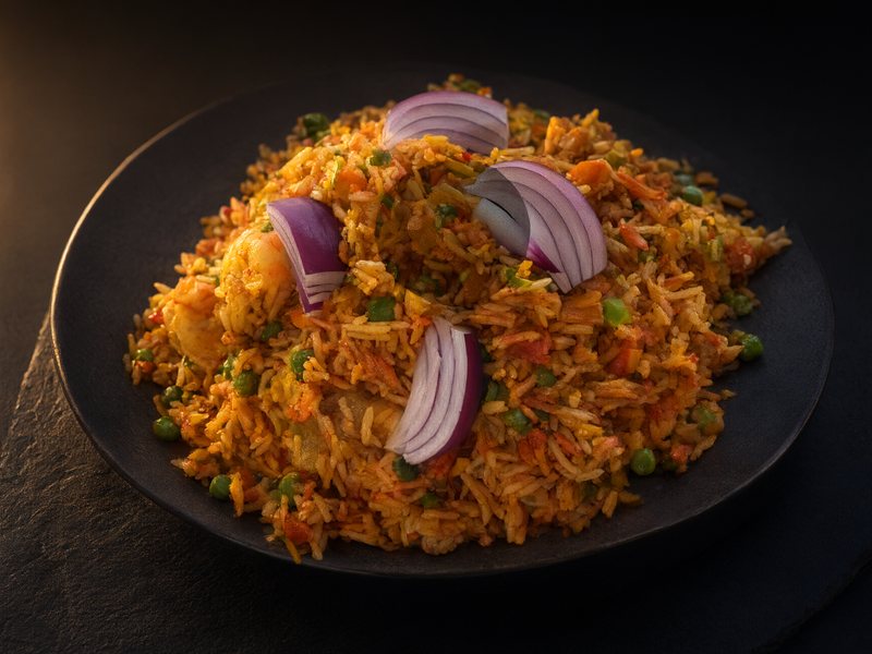 Shrimp fried rice with peas, carrot and slices of red onion on a dark plate