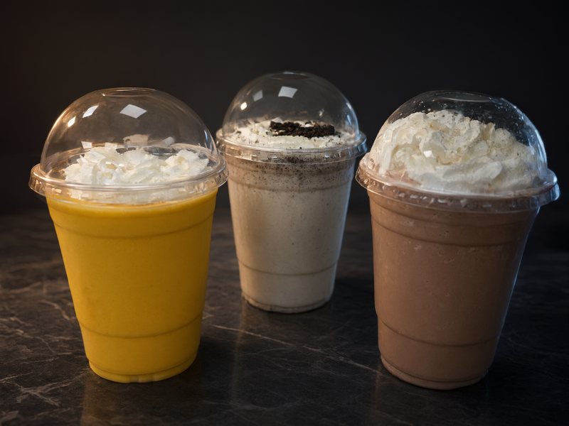 Three shakes with whipped cream under clear dome lids: mango, cookies and cream, and chocolate