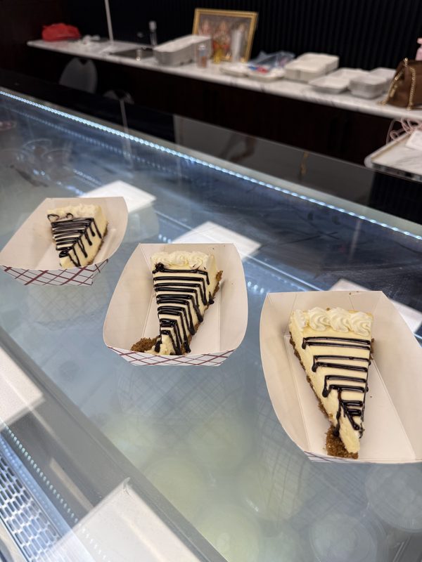 Three slices of striped cheesecake in paper trays on the glass counter