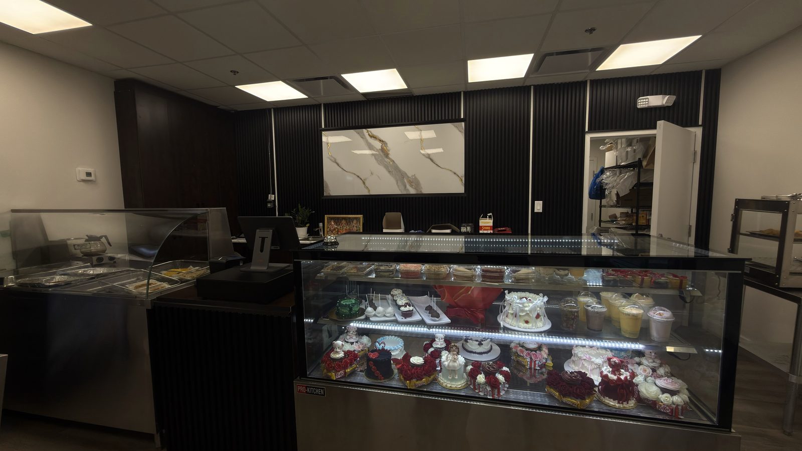The counter at Nisha's Culinary: black slat wall, marble panel and the lit cake case